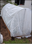 A floating row cover and hoop structure over a garden bed.